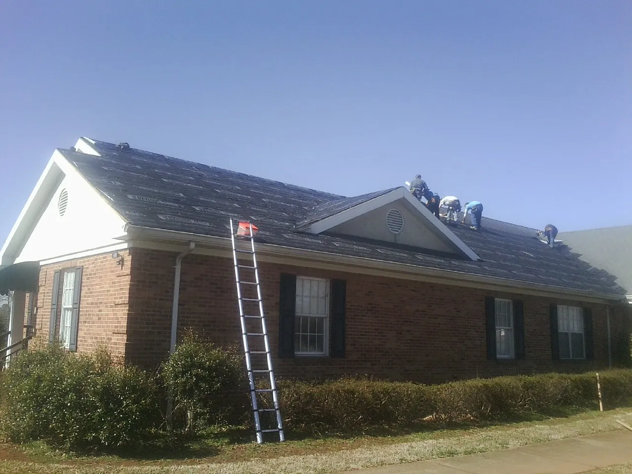 Crew tearing shingles off a brick ranch roof with a ladder set — Emergency Roof Repair work by our crew in Hephzibah