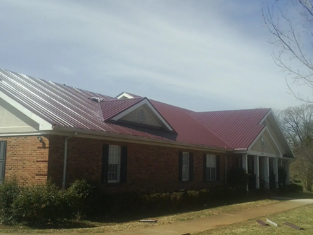 Red metal roof with gabled entries on a long brick building, from a Hail Damage Roof Repair job in Hephzibah