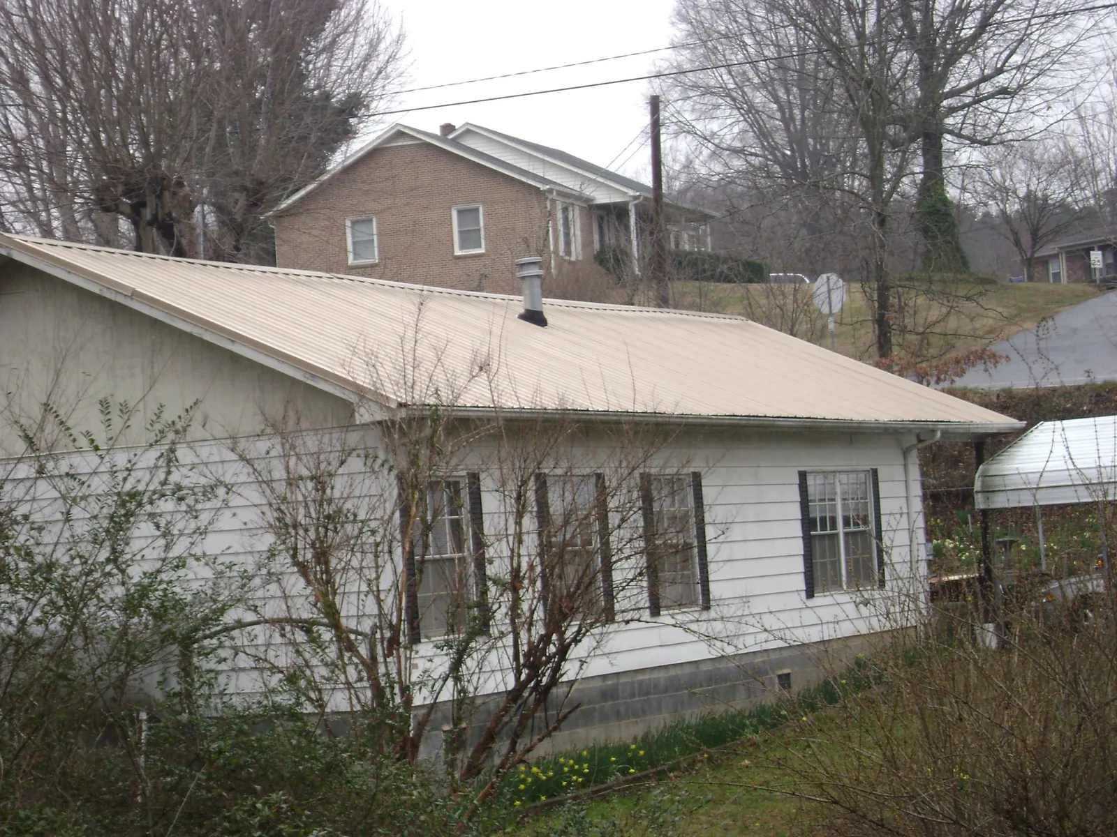 Tan metal roof on a white sided house set into a hillside — Commercial Roofing by Roofing Brothers in Hephzibah